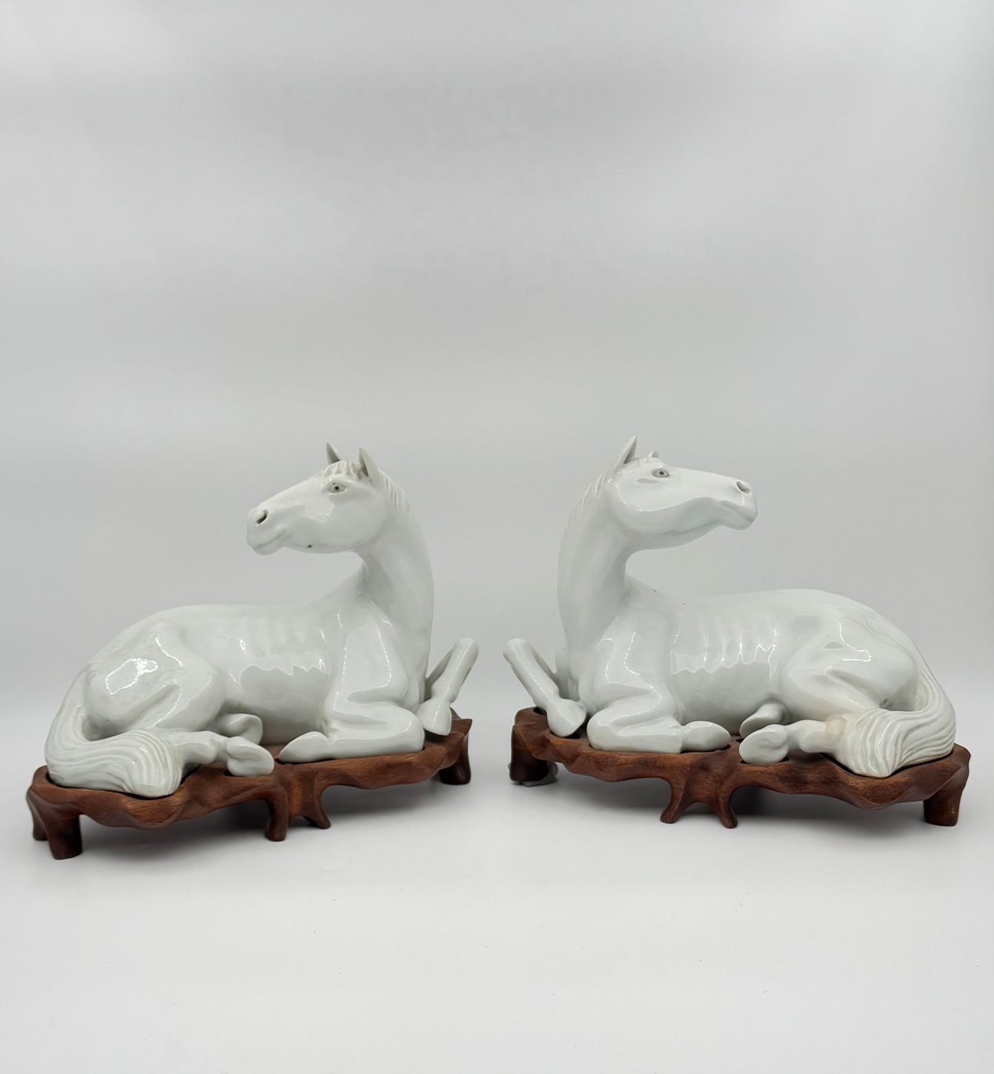 Pair of Chinese Blanc de Chine Porcelain Recumbent Horses on Carved Wood Stands