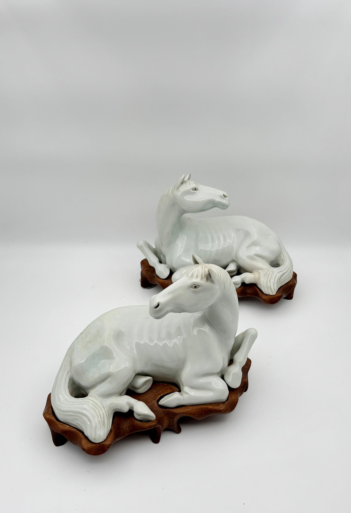 Pair of Chinese Blanc de Chine Porcelain Recumbent Horses on Carved Wood Stands