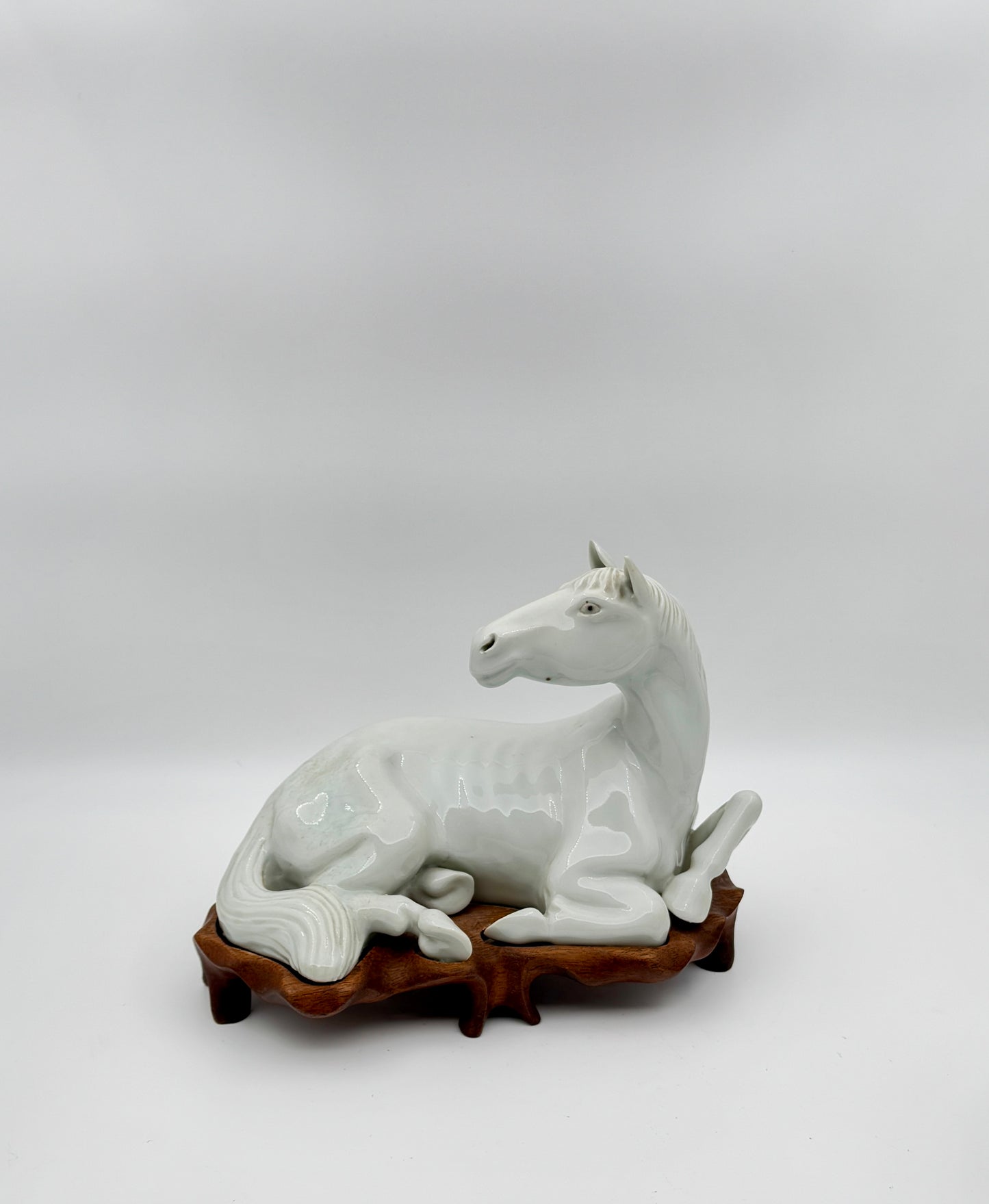 Pair of Chinese Blanc de Chine Porcelain Recumbent Horses on Carved Wood Stands