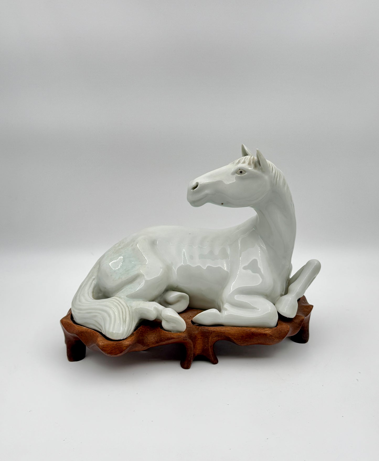 Pair of Chinese Blanc de Chine Porcelain Recumbent Horses on Carved Wood Stands