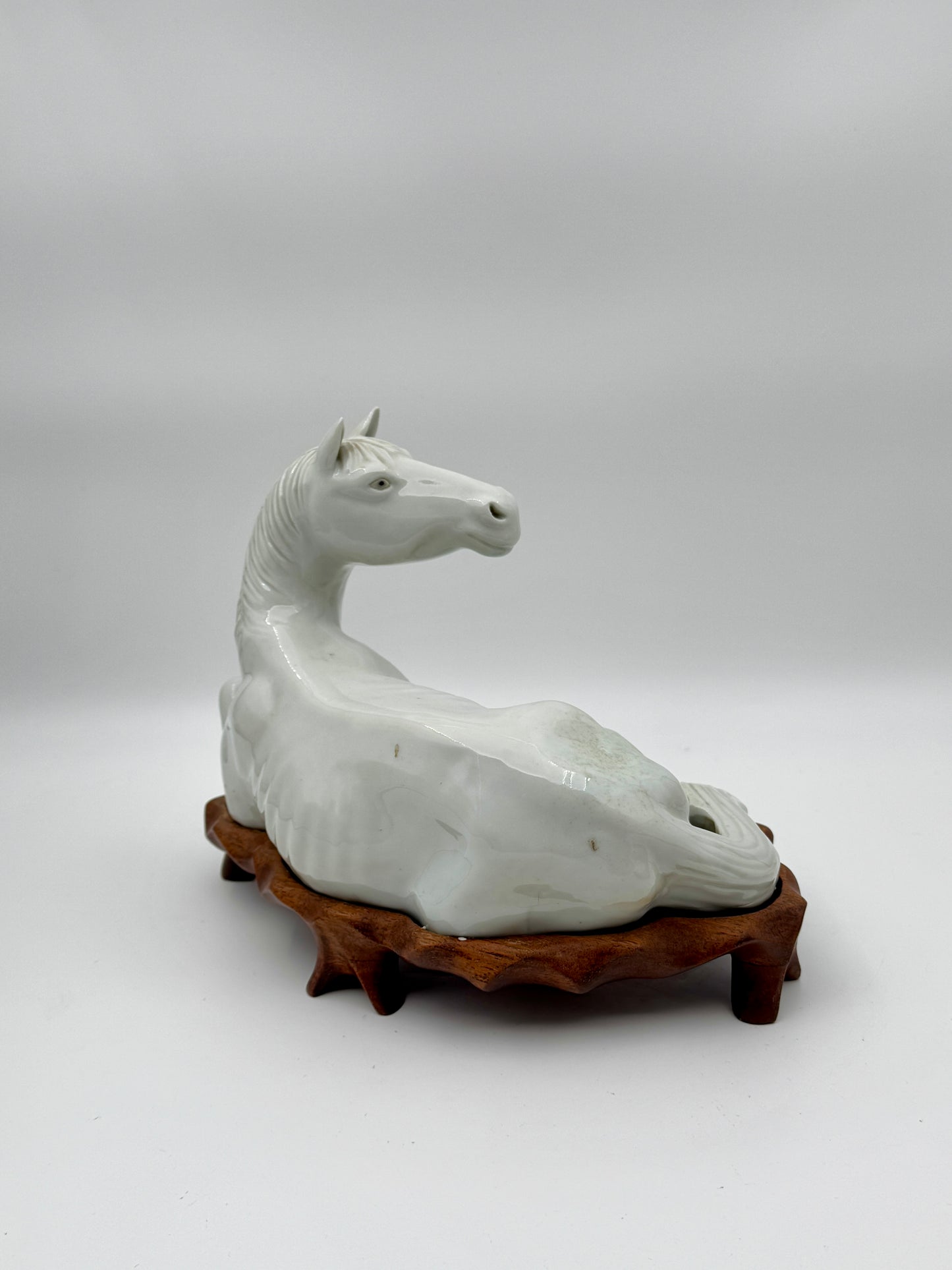 Pair of Chinese Blanc de Chine Porcelain Recumbent Horses on Carved Wood Stands