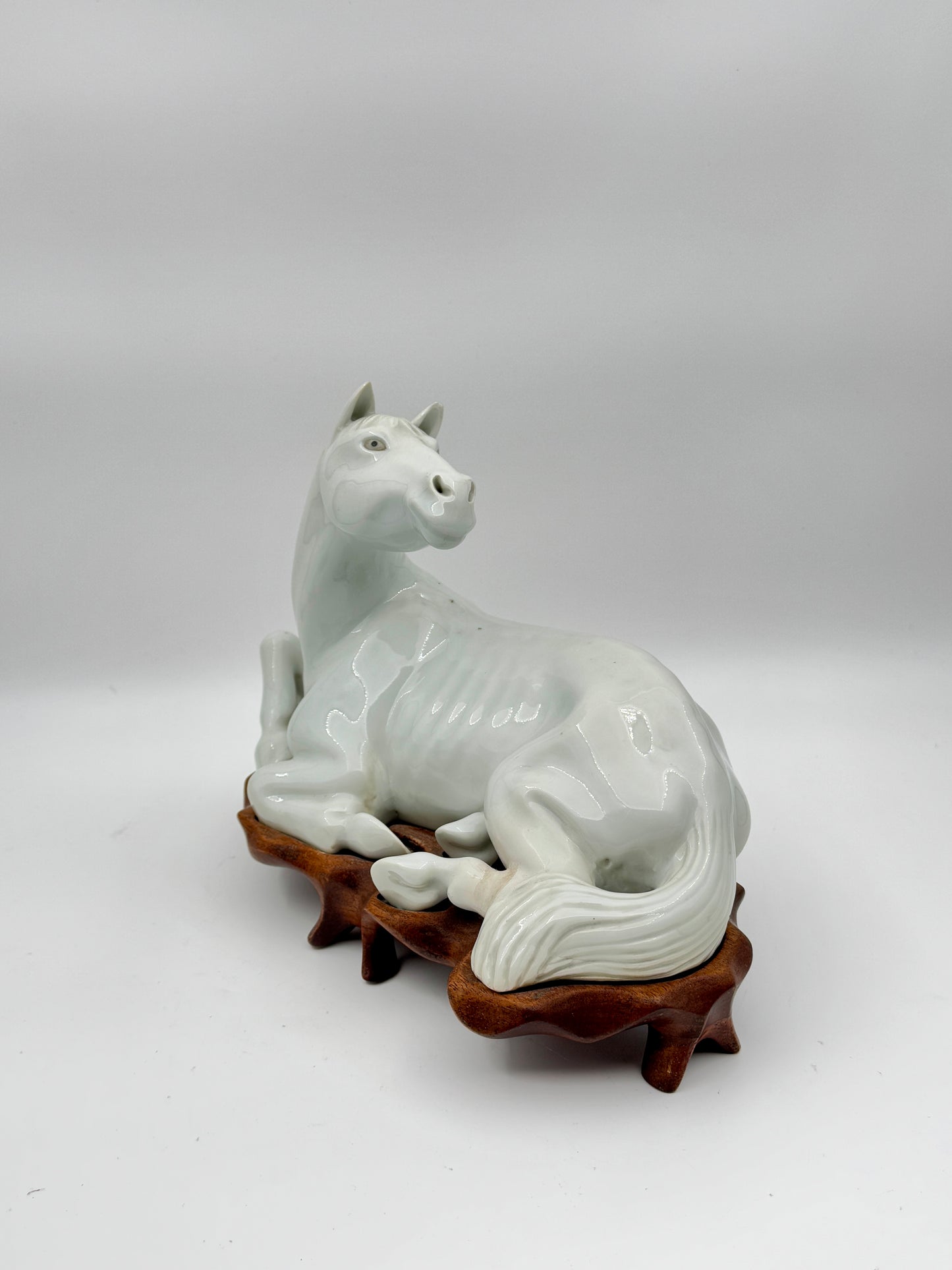 Pair of Chinese Blanc de Chine Porcelain Recumbent Horses on Carved Wood Stands